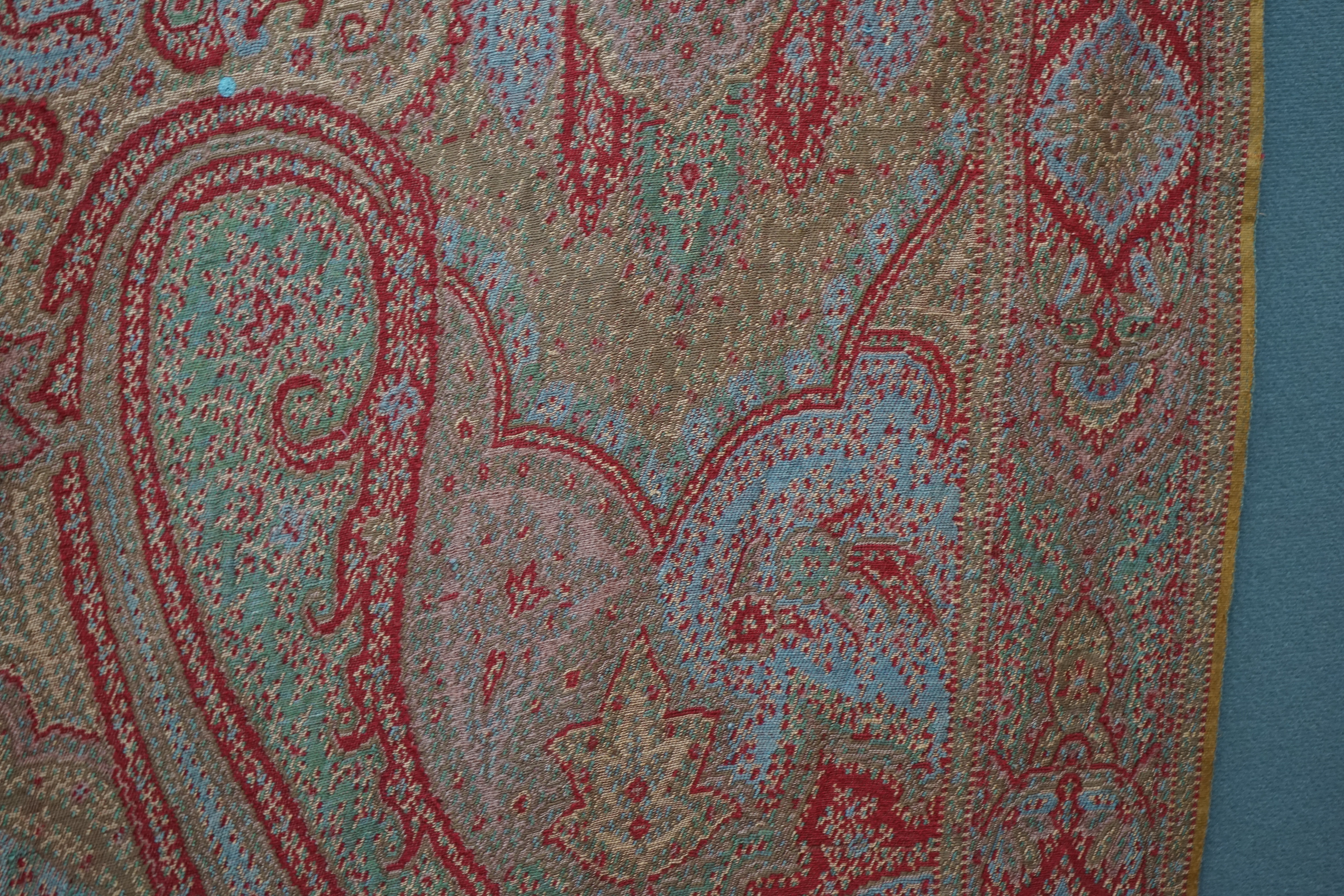 A 19th century wool and silk woven Paisley shawl, woven in a diagonal tear drop design, in reds, blues, greens, creams and ochres, with an all round woven border, tasselling both ends, 320cm long x 162cm wide. Condition